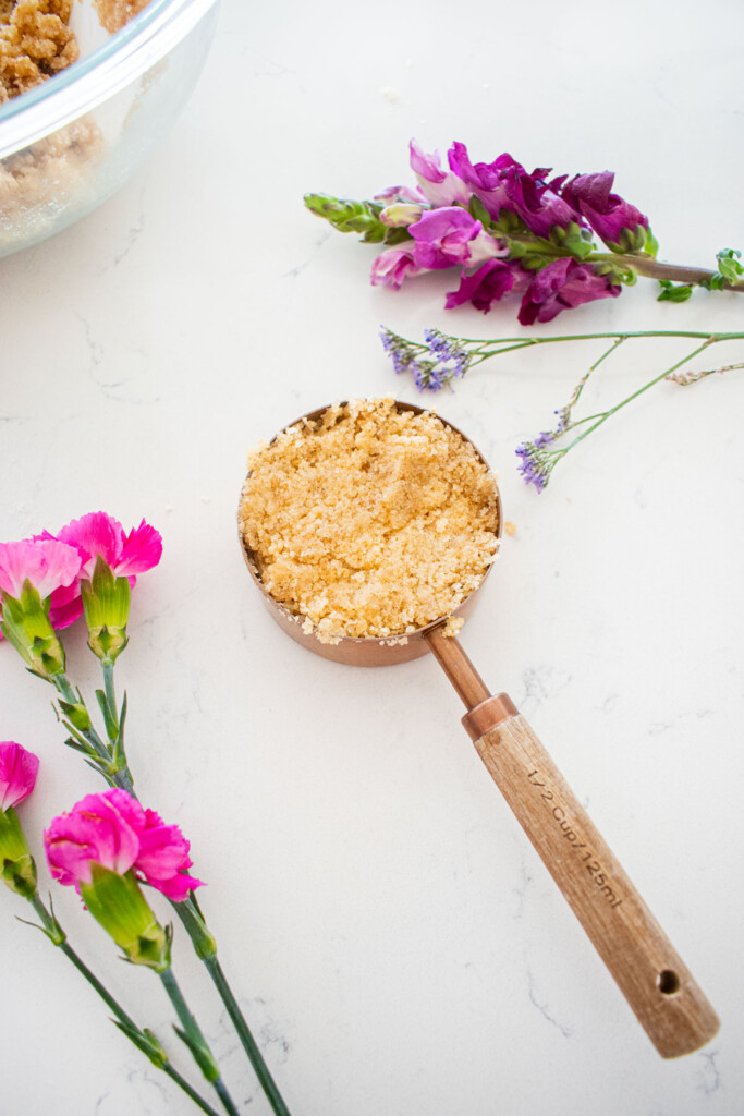 half cup of cherry pie bar dough in a measuring cup on a white marble counter with fresh flowers.