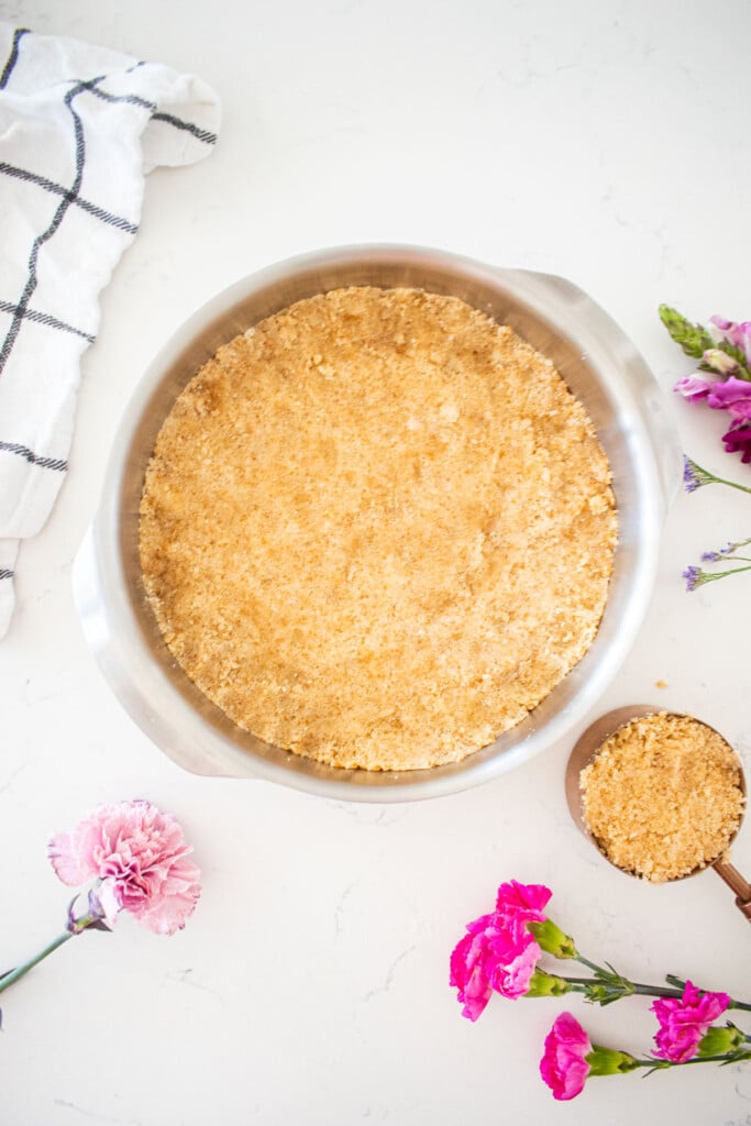cherry pie bar dough in a 8-inch round pan pressed flat on a white marble counter with fresh flowers.