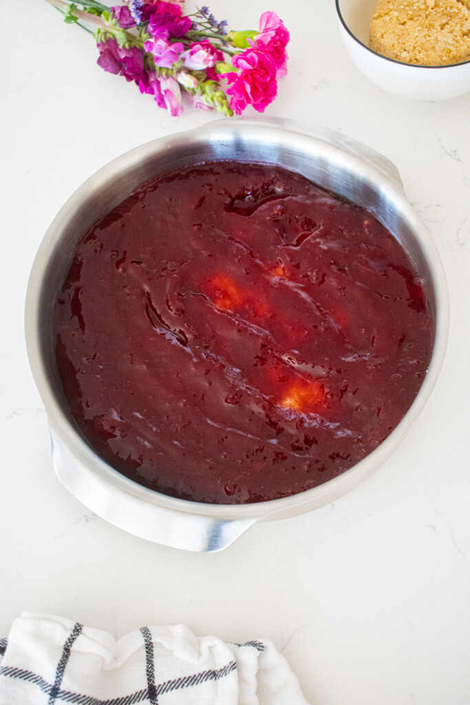 round cake pan with cherry pie jam spread into it on a white marble counter with fresh flowers.
