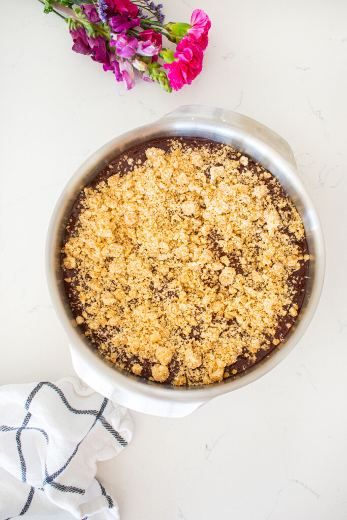 round cake pan with cherry jam and crumb topping on a white marble counter with fresh flowers.