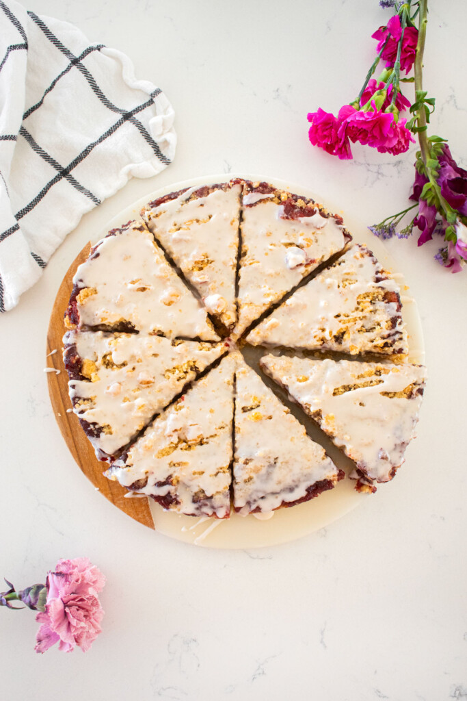 cherry pie bars with glaze cut into triangles on a white marble counter with fresh flowers.