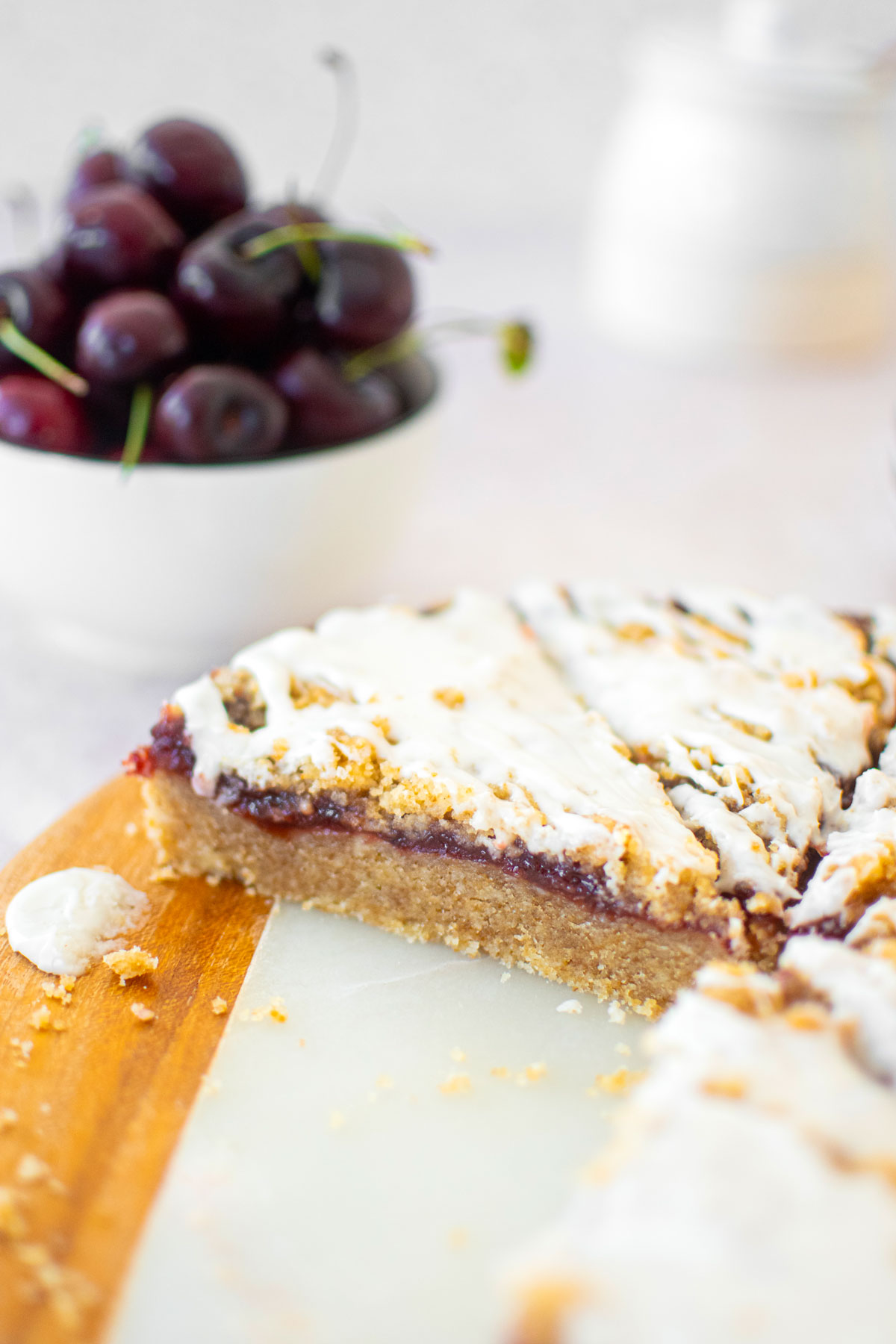cherry pie bars cut into triangles on a round marble serving board with fresh cherries.
