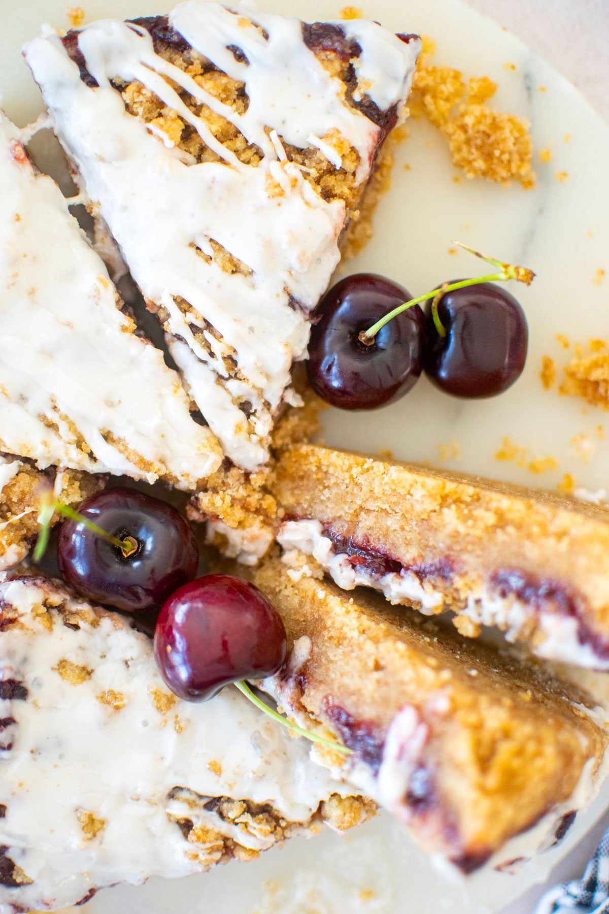 cherry pie bars cut into triangles on a round marble serving board with fresh cherries.