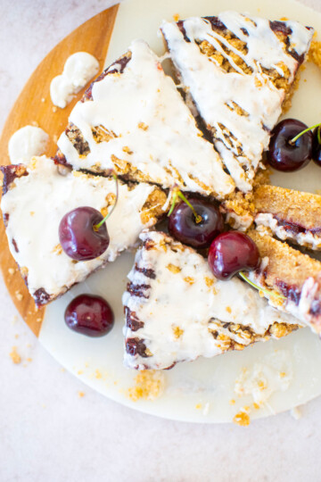 cherry pie bars cut into triangles on a round marble serving board with fresh cherries.
