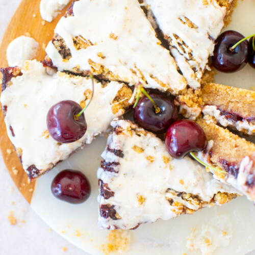 cherry pie bars cut into triangles on a round marble serving board with fresh cherries.