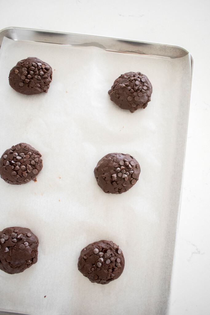 chocolate espresso cookie dough balls on a baking sheet on a marble counter.