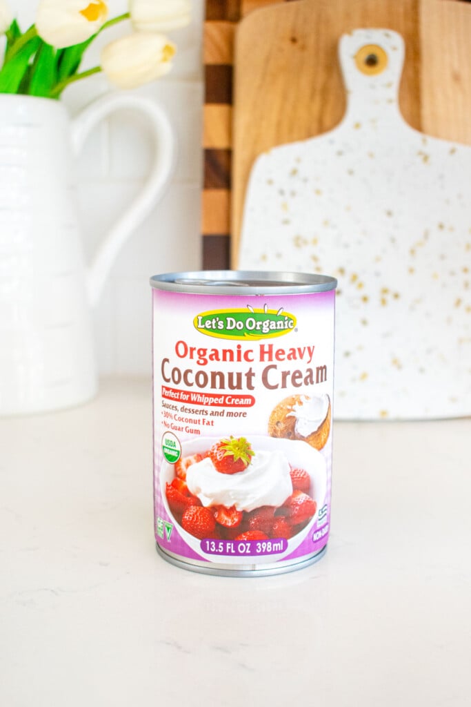 can of organic coconut cream on a white marble counter with fresh flowers.