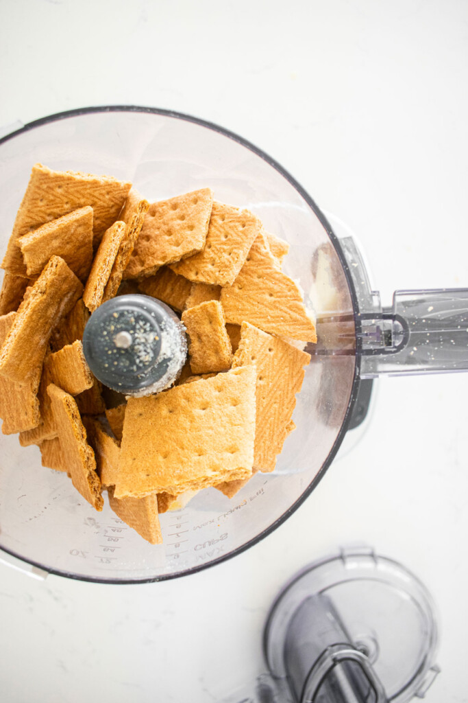 graham crackers in a food processor on a white marble counter.