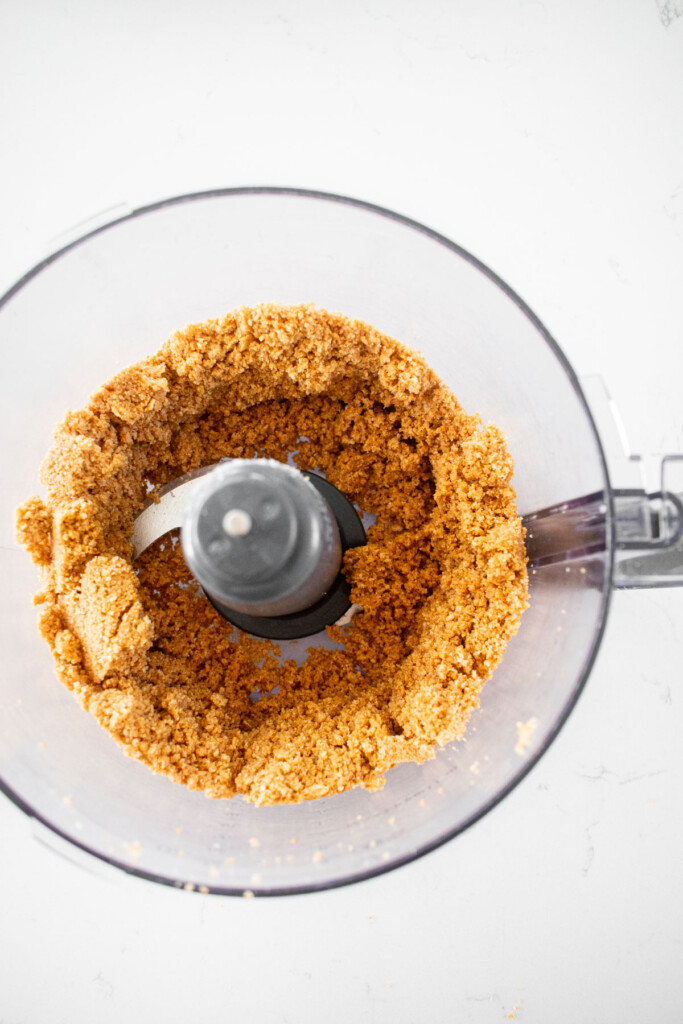 graham cracker crust in a food processor on a white marble counter.