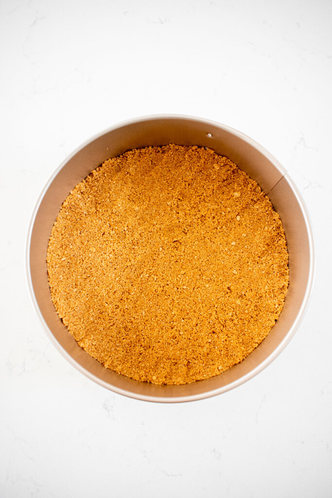 graham cracker crust in a springform pan on a white marble counter.