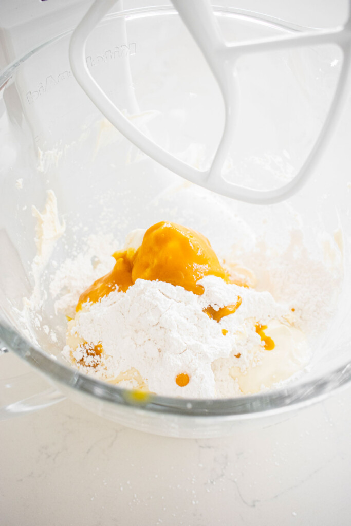 ingredients for mango cheesecake in a glass mixing bowl on a white marble counter.