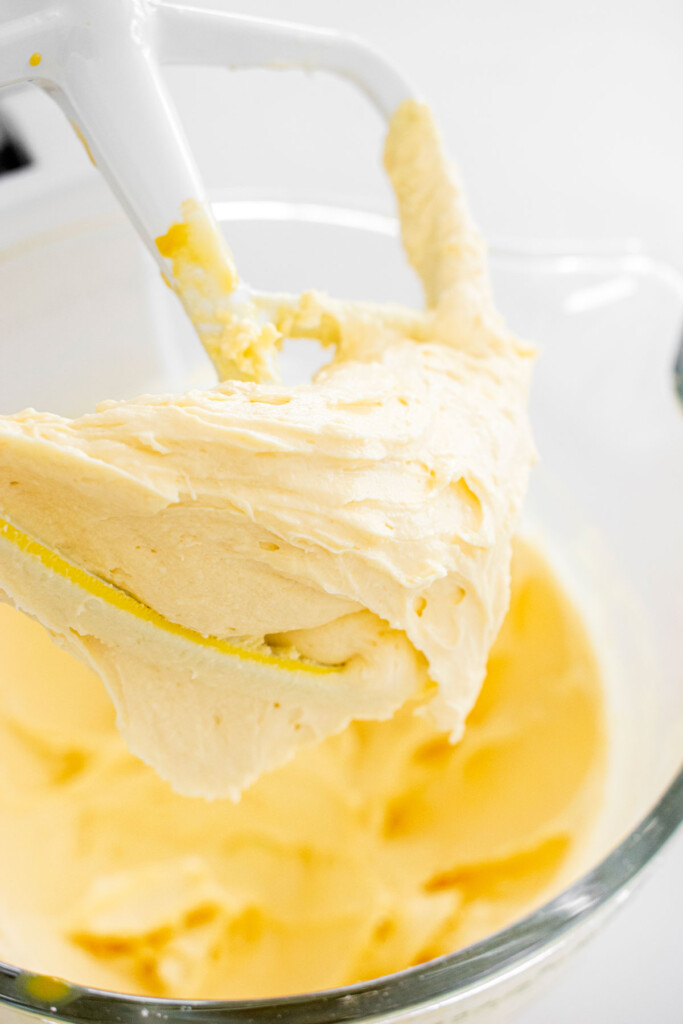 mango cheesecake filling in a glass mixing bowl on a white marble counter.