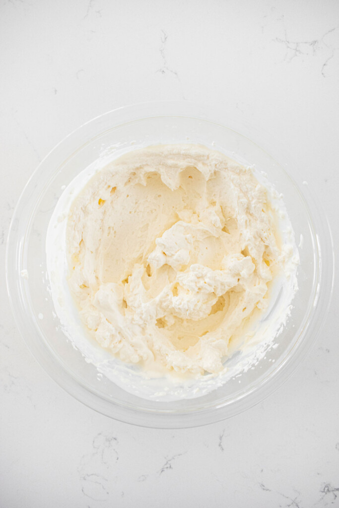 whipped cream in a glass mixing bowl on a white marble counter.