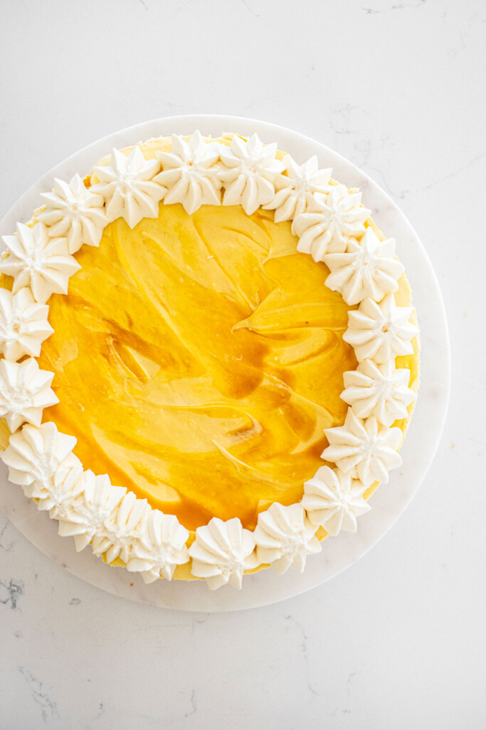 easy mango cheesecake with whipped cream dollops around the edges on a white marble counter.