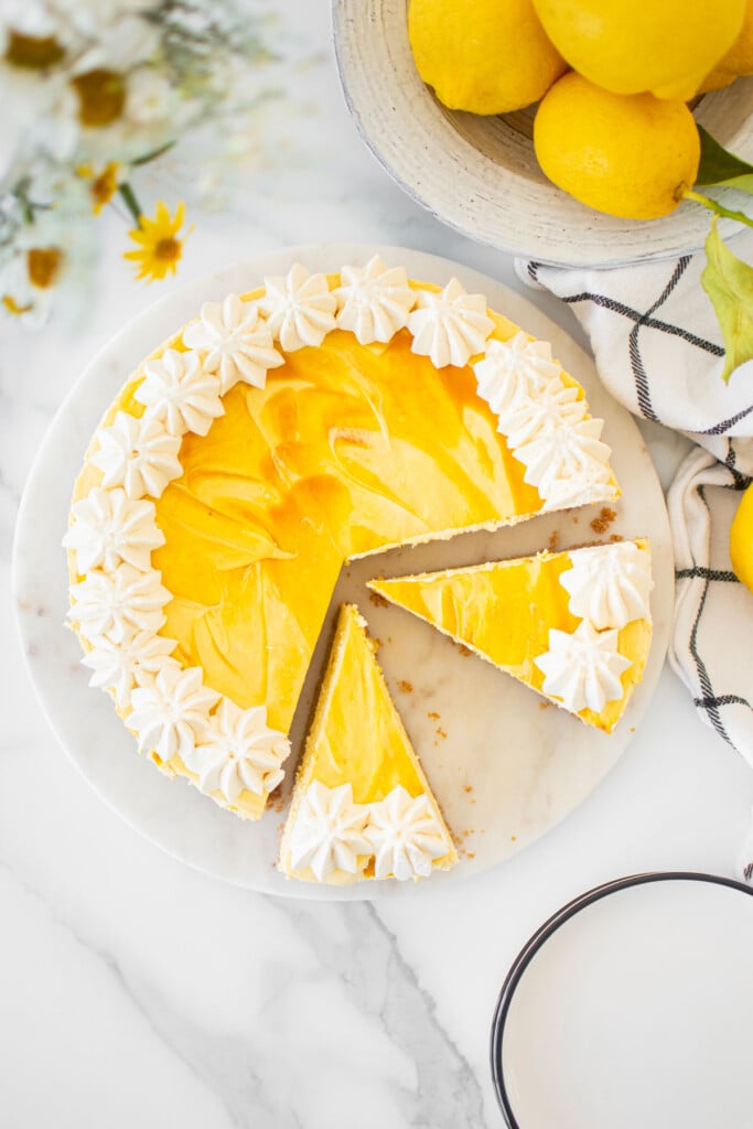 easy mango cheesecake cut into slices on a white marble serving board on a marble table with fresh flowers and lemons.