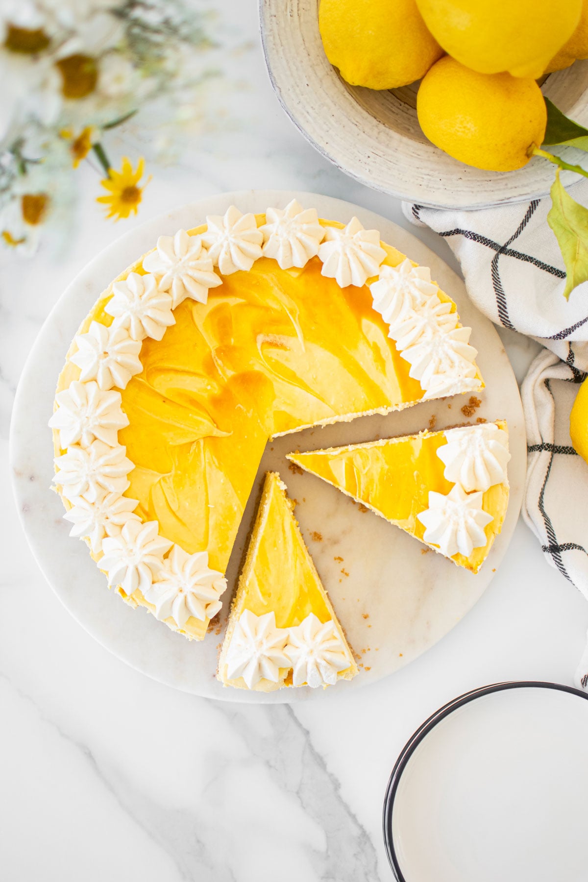 easy mango cheesecake cut into slices on a white marble serving board on a marble table with fresh flowers and lemons.