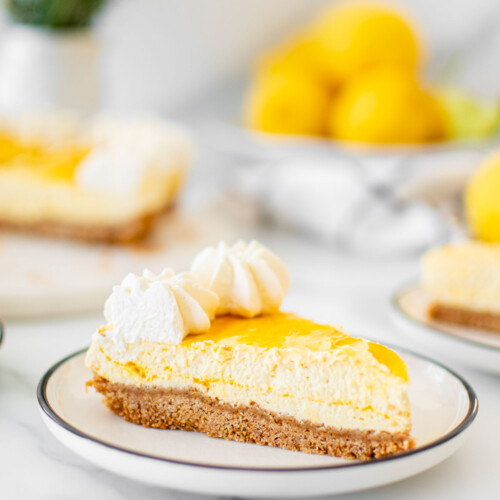 slice mango cheesecake on a plate on a white marble table with fresh lemons and flowers.