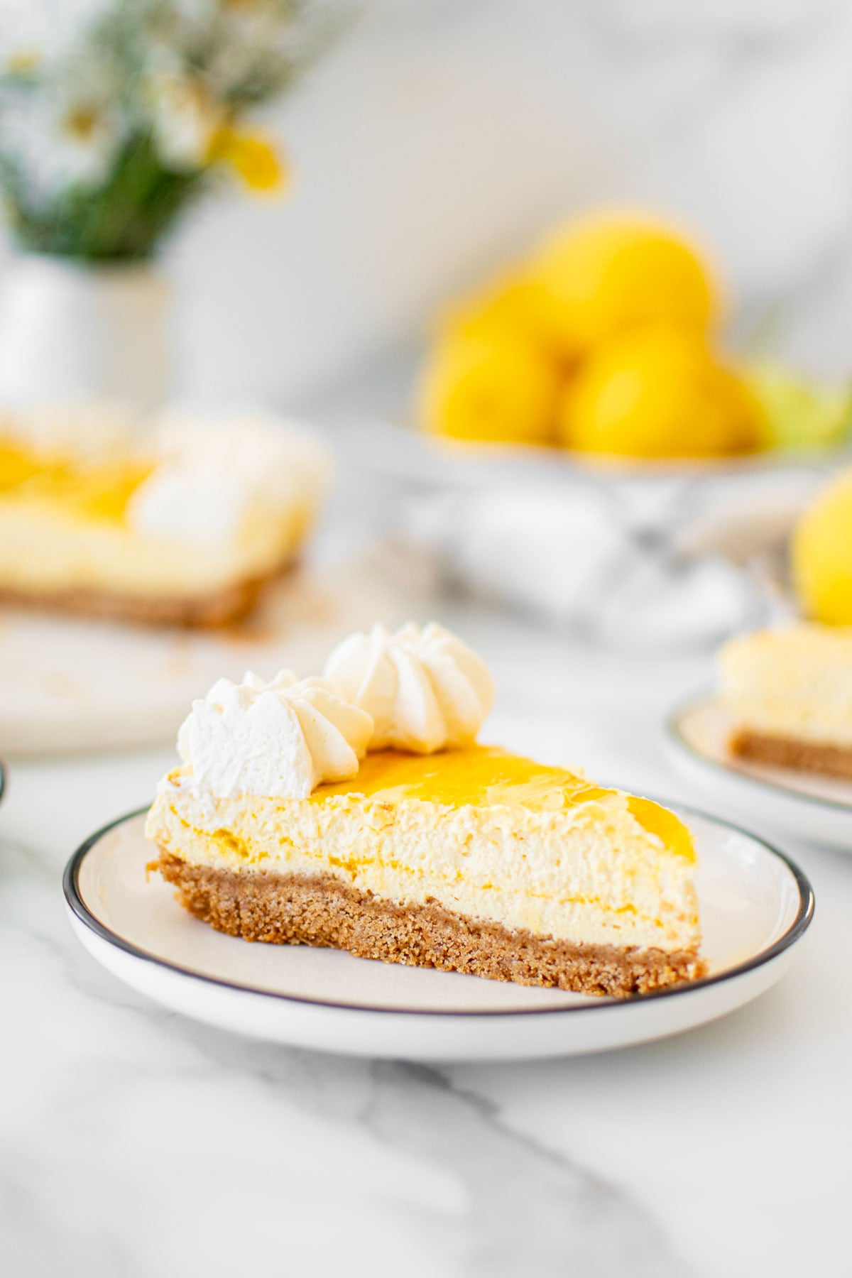 slice mango cheesecake on a plate on a white marble table with fresh lemons and flowers.