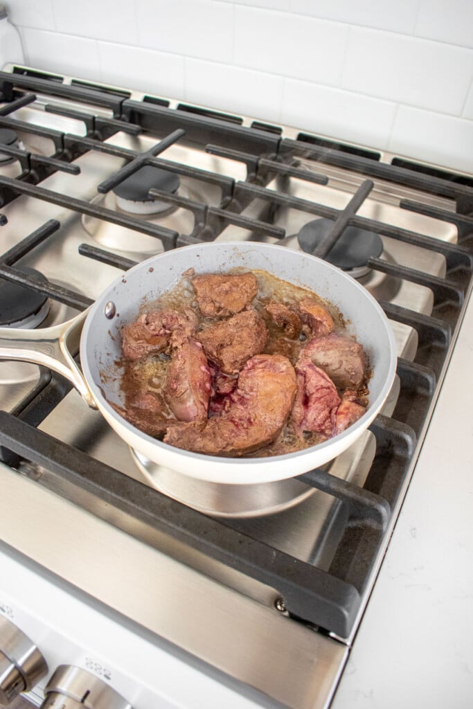 beef liver cooking in a skillet on the stovetop.