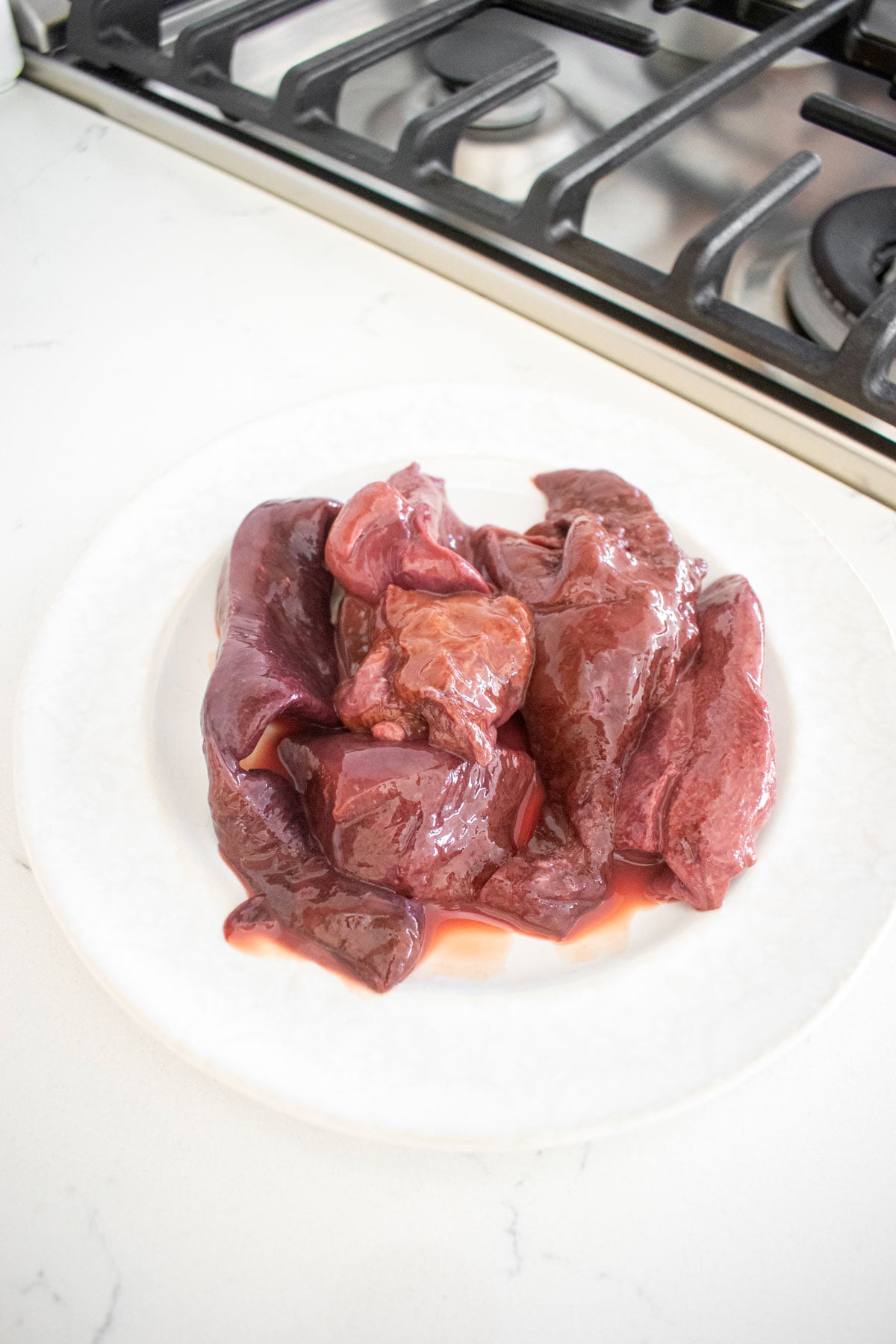 raw beef liver on a plate on the counter next to the stove.