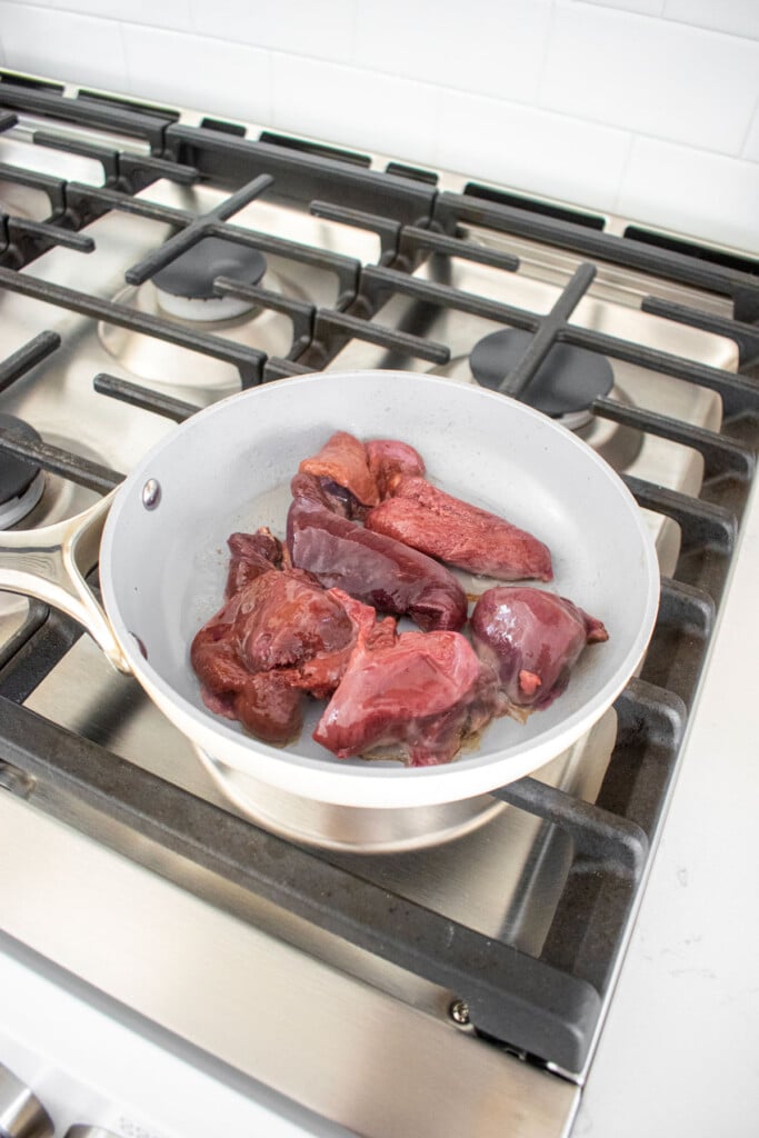 beef liver in a skillet on the stovetop cooking.