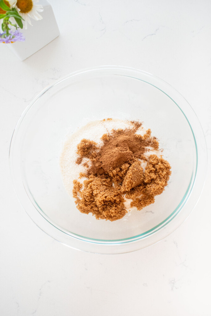 sugar, brown sugar and flour in a glass mixing bowl on a marble counter.