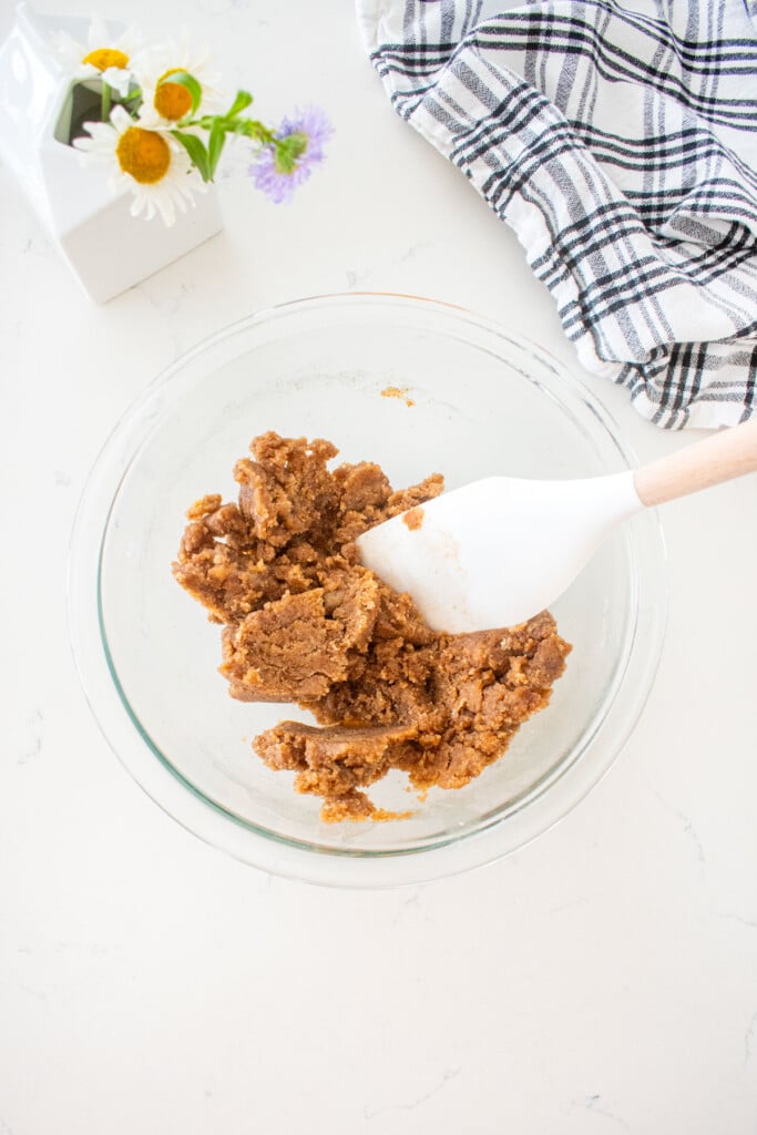 crumb topping mixed together in a glass mixing bowl on a marble counter with fresh flowers.