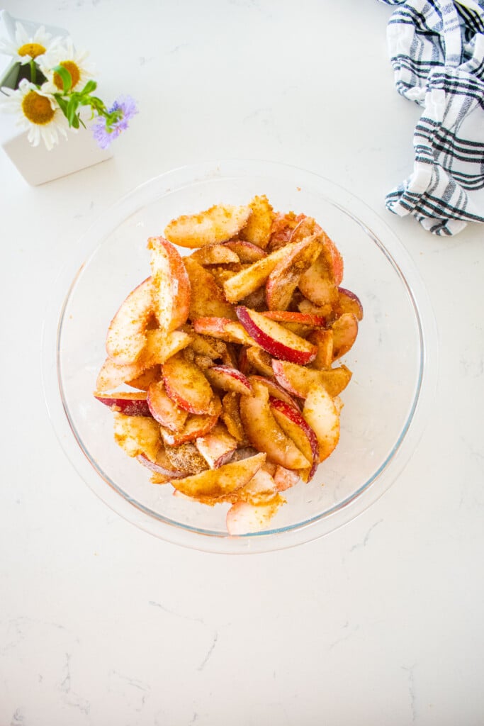 peach pie filling mixed together in a glass mixing bowl on a marble counter with a vase of fresh flowers.