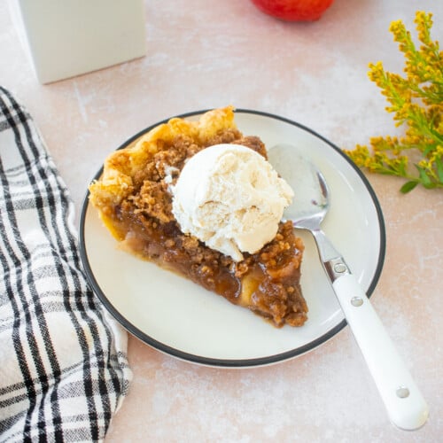 slice of peach crumble pie with vanilla ice cream on top on a plate on a table with fresh flowers.