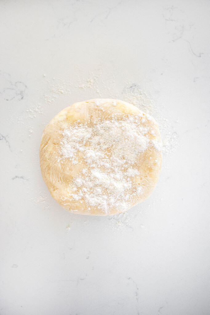 pie crust on a white marble countertop with a little flour on top.