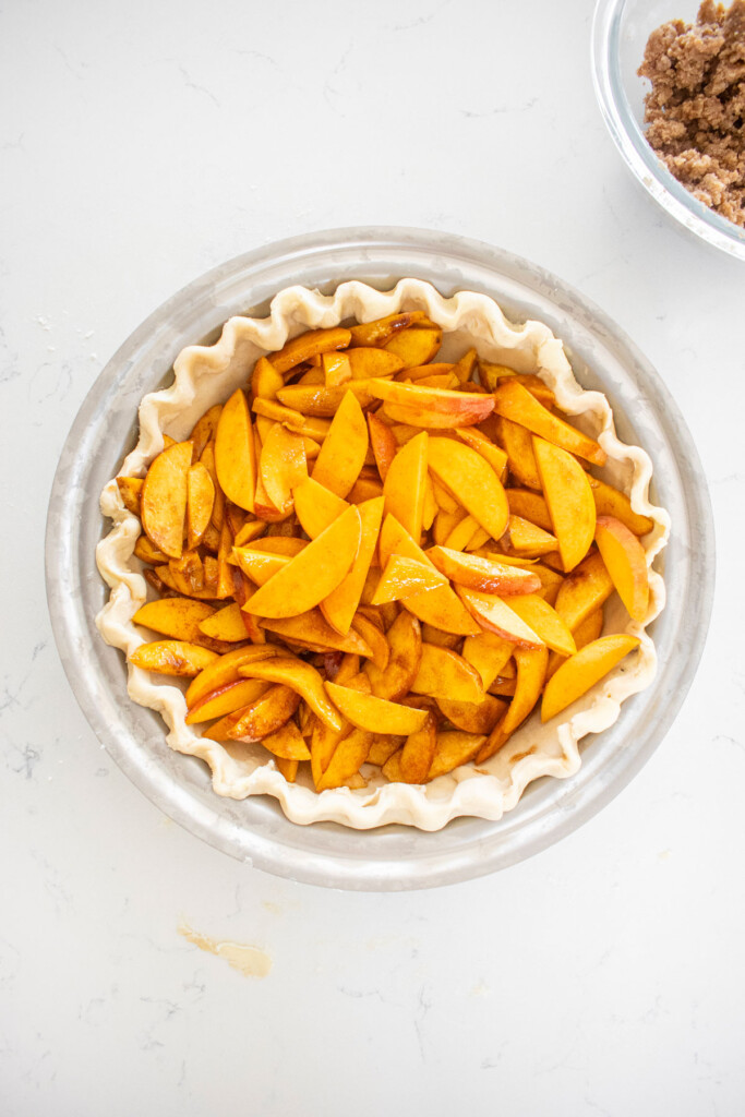 peach pie in a pie crust in a stainless steel pie pan on a white marble counter.