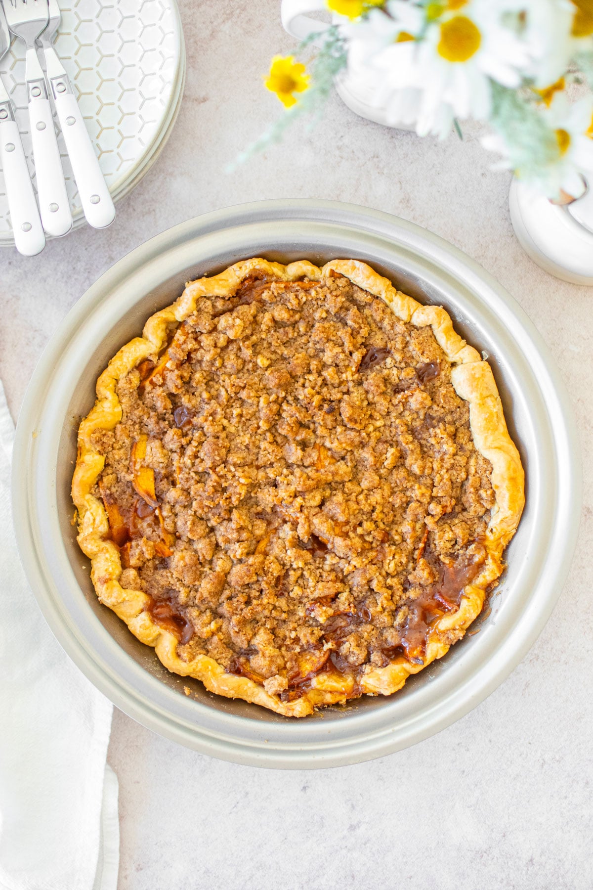 peach crumble pie in a stainless steel pan with fresh flowers.