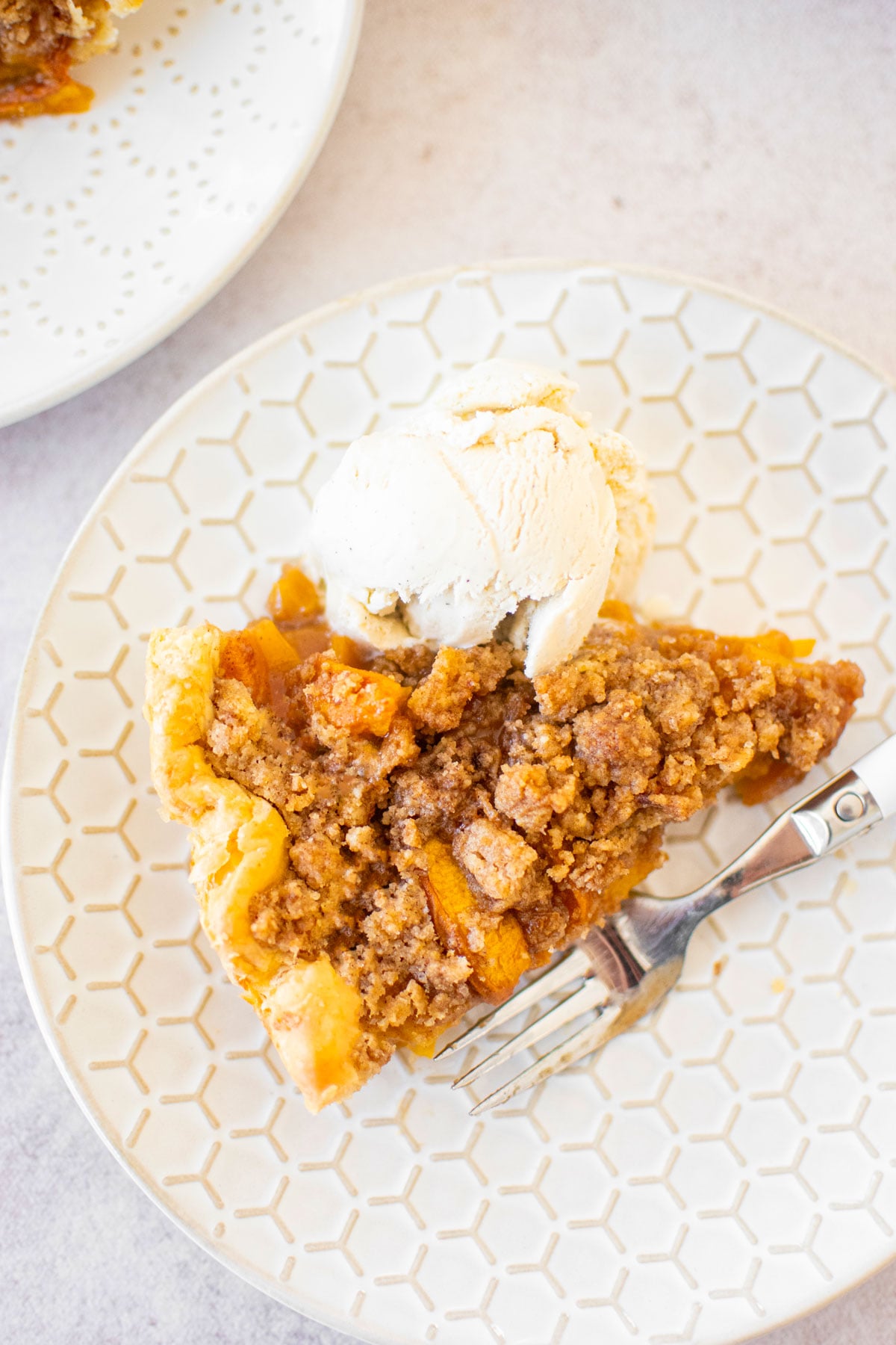 slice of peach crumble pie with a scoop of vanilla ice cream on a white plate.