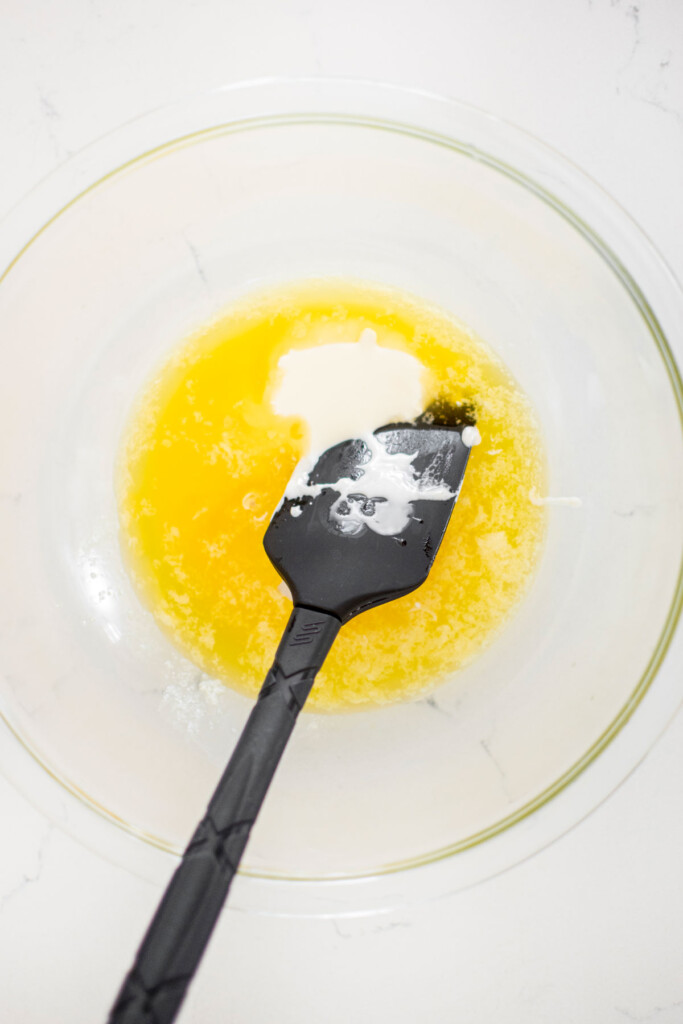 melted butter and sourdough discard in a glass mixing bowl with a spatula on a white marble counter.