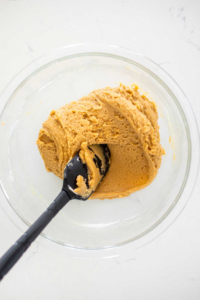 sourdough cookie dough with a spatula in a glass mixing bowl on a white marble counter.