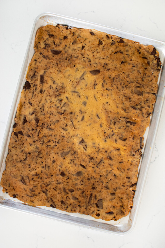 half sheet pan pressed with sourdough chocolate chip cookie dough on a white marble counter.