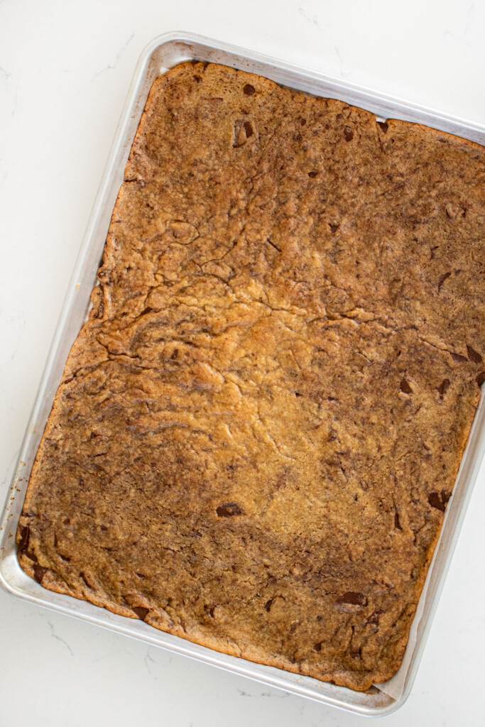 baked sourdough chocolate chip cookie dough on a baking sheet on a marble counter.