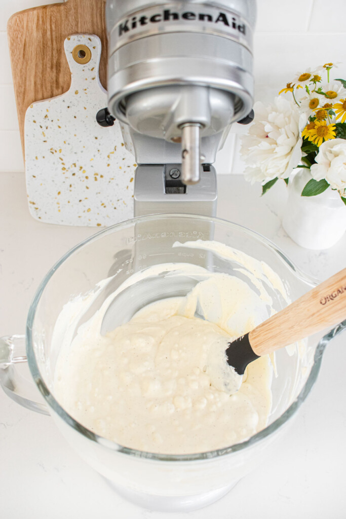 no churn vanilla ice cream mixed in a glass stand mixing bowl on a white marble counter.