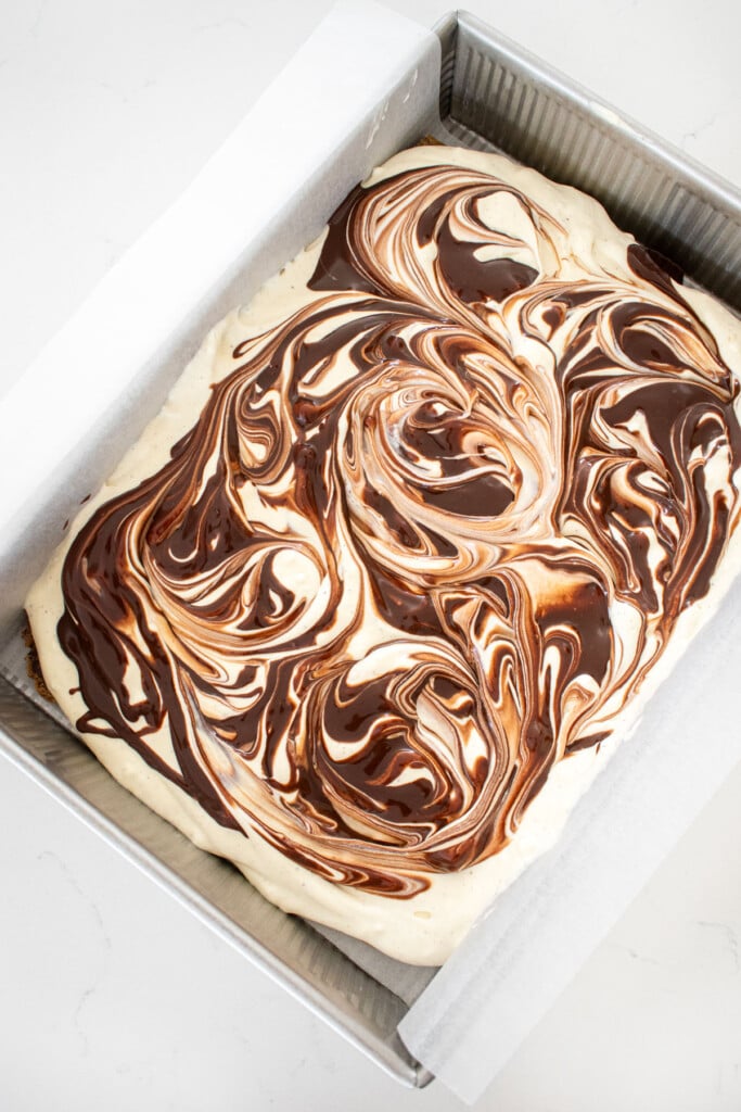 chocolate ganache swirled on top of vanilla ice cream in a baking pan on a white marble counter.