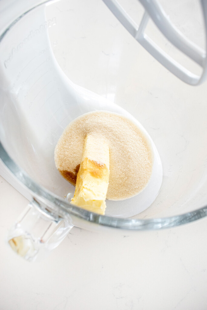 butter sugar and vanilla in a glass mixing bowl on a white marble counter.