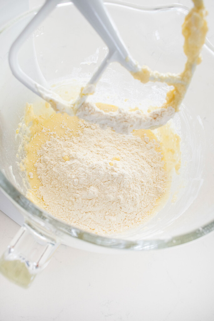 ingredients for vanilla cake in a glass mixing bowl on a white marble counter.
