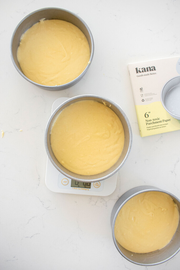 vanilla cake batter in three 6-inch cake pans on a white marble counter.