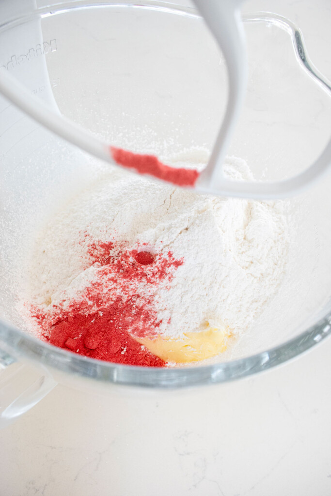 ingredients for strawberry buttercream in a glass mixing bowl on a white marble counter.