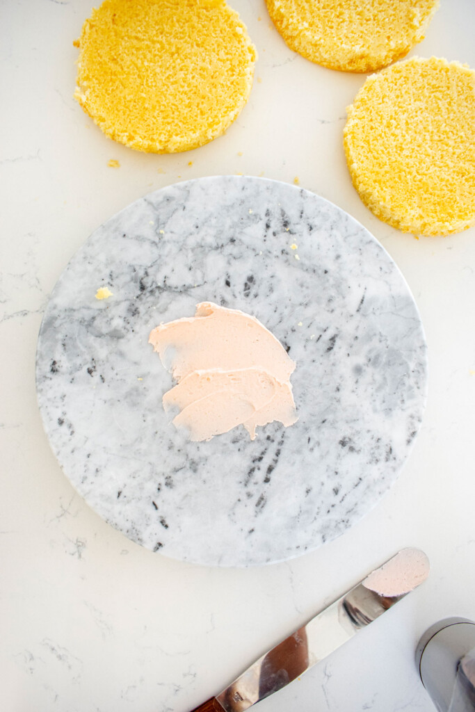 marble cake spinner with pink frosting on top on a white marble counter with vanilla cake layers.