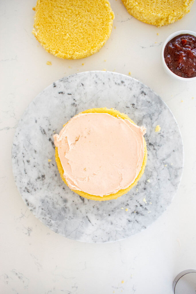 vanilla layer cake being assembled on a marble cake spinner with strawberry frosting.