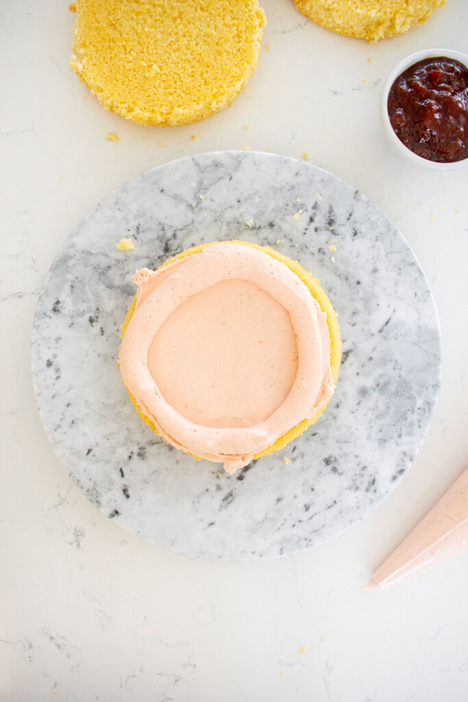 pink strawberry buttercream being frosted on a vanilla layer cake on a marble cake spinner.
