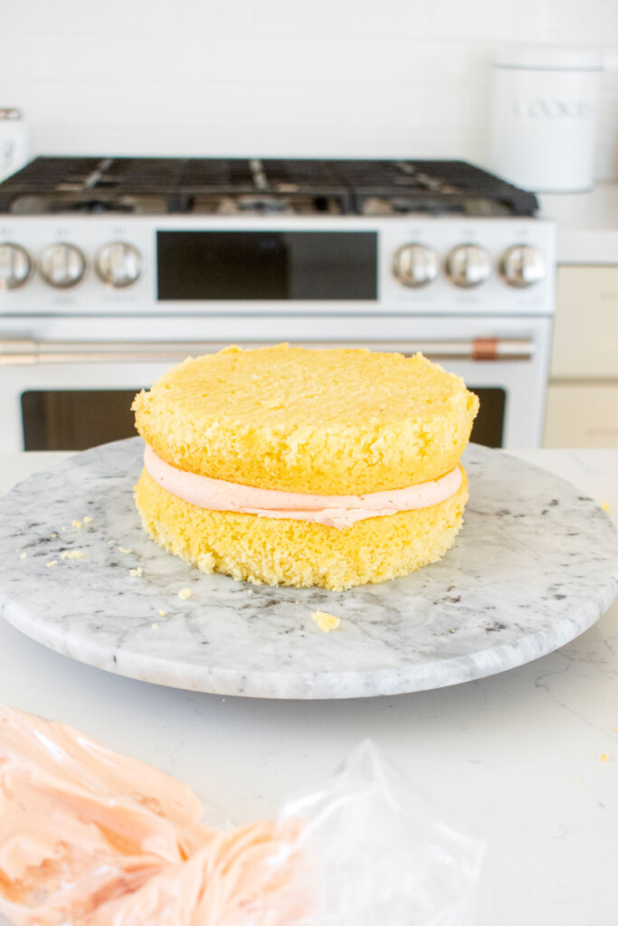 vanilla layer cake being assembled on a marble cake spinner with strawberry frosting.
