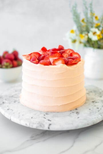 strawberry vanilla layer cake on a marble cake plate on a white marble table with fresh flowers.