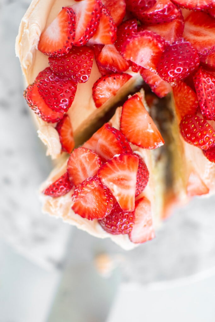 strawberry vanilla layer cake with fresh strawberries with a slice cut out on a marble cake plate.