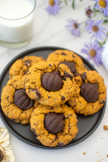 brown butter pumpkin cookies with caramel on a plate with a glass of milk and fresh flowers on a marble counter.
